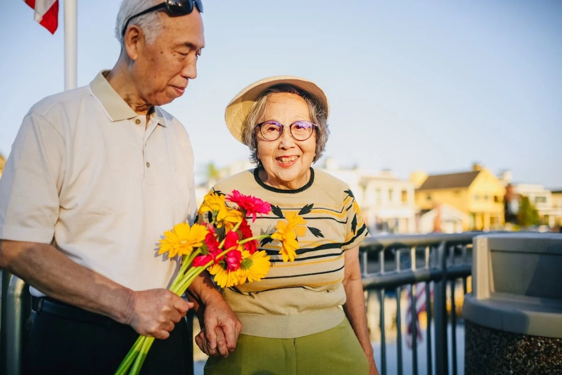 old couple, man is holding flowers and the woman is smiling